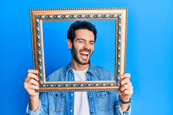 Joven Hombre Hispano Sosteniendo Marco Vacío Sonriendo Riendo Voz Alta — Foto de Stock