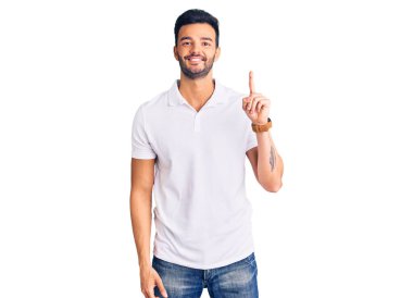 Gündelik kıyafetler giyen genç, yakışıklı İspanyol bir numarayı gösterip işaret ederken kendinden emin ve mutlu bir şekilde gülümsüyor.. 