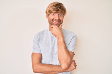 Gündelik giysiler giyen genç bir adam kameraya kendinden emin bakıyor kollarını kavuşturup gülümsüyor ve çenesini kaldırıyor. Olumlu düşünmek. 