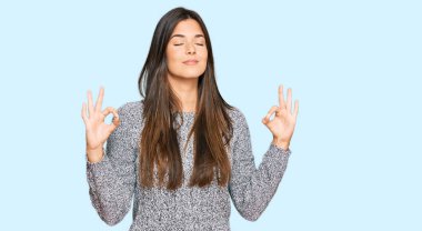 Kış süveteri giyen genç esmer kadın rahatla ve gözleri kapalı gülümse parmaklarıyla meditasyon hareketi yapıyor. yoga konsepti. 