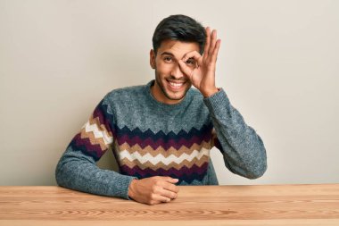 Genç, yakışıklı bir adam, sıradan bir süveter giyip masada oturuyor. El hareketleriyle gülümsüyor, gözleriyle mutlu yüzüyle parmaklarının arasından bakıyor.. 