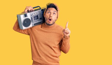 Yakışıklı Latin Amerikalı genç adam kasetçalar tutuyor, müzik dinliyor şaşkın şaşkın yukarı bakıyor ve parmaklarıyla işaret ediyor ve kollarını kaldırıyor.. 