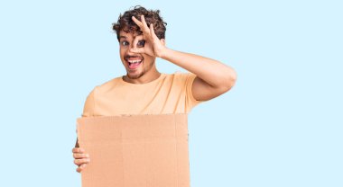 Genç, kıvırcık saçlı, elinde boş karton pankart olan yakışıklı, mutlu mesut gülümseyen, el pençe divan duran, el pençe divan duran bir adam. 