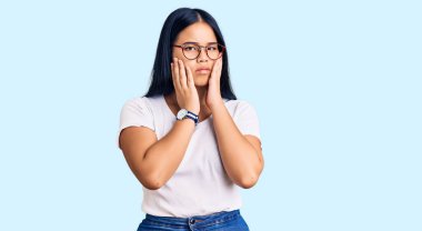 Genç ve güzel Asyalı kız günlük kıyafetler ve gözlük takıyor. Yorgun eller yüzünü kapatıyor. Depresyon ve üzüntü içinde. 