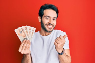 İspanyol asıllı genç adam 10 pound tutuyor. Banknotlar gururla haykırıyor, zaferi ve başarıyı kutluyor. 