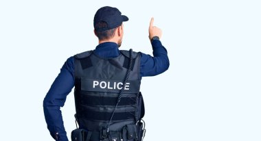 Polis üniforması giyen genç ve yakışıklı bir adam geriye doğru poz veriyor. 