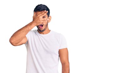 Gündelik kıyafetler giyen genç Latin adam şok içinde yüzünü ve gözlerini kapayarak utanmış ifadesiyle parmaklarının arasından bakıyor.. 