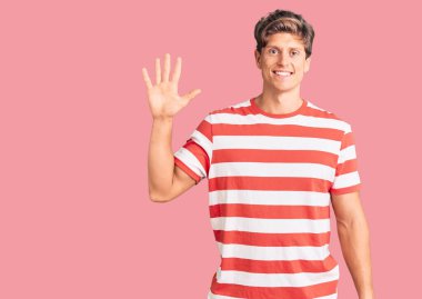 Gündelik kıyafetler giyen genç yakışıklı adam beş numarayı gösterip işaret ederken kendinden emin ve mutlu bir şekilde gülümsüyor.. 