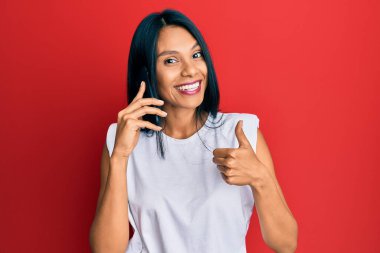 Genç Afro-Amerikalı kadın akıllı telefondan konuşuyor mutlu ve olumlu gülümsüyor, başparmağıyla mükemmel ve onay işareti yapıyor. 