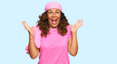 Orta yaşlı İspanyol kadın göğüs kanseri desteği takıyor. Pembe eşarp zaferi kutluyor. Gülümsüyor ve ellerini kaldırarak kazanan yüz ifadesi sergiliyor. 