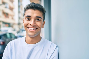 Genç Latin adam gülümsüyor. Şehrin duvarına yaslanmış mutlu bir şekilde..