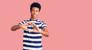 Genç Afro-Amerikalı sıradan kıyafetler giyen, aşık gülümseyen, elleriyle kalp sembolü yapan bir adam. romantik kavram. 