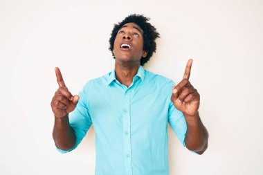 Yakışıklı Afro saçlı, sıradan giyinmiş, afili bir Amerikalı. Şaşırmış ve şaşırmış bir şekilde yukarı bakıyor, parmaklarıyla işaret ediyor ve kolunu kaldırıyor.. 