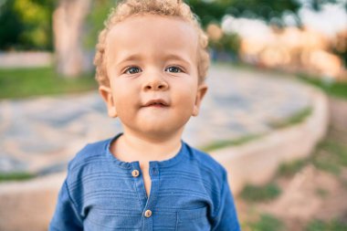 Sevimli ve mutlu küçük çocuk güneşli bir günde parkta eğleniyor. Güzel sarı saçlı erkek çocuk dışarıda oynuyor.