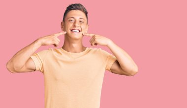 Gündelik kıyafetler giyen, neşeli gülümseyen, parmaklarıyla ve ağzıyla işaret eden genç yakışıklı bir adam. diş sağlığı kavramı. 