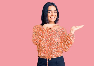 Gündelik giysiler giyen genç ve güzel Latin kadın kameraya hayret ediyor ve gülümsüyor.. 