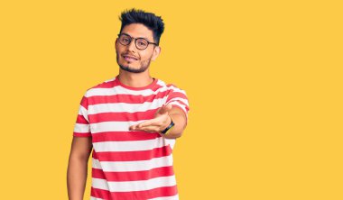 Yakışıklı Latin Amerikalı gündelik kıyafetler ve gözlük takan neşeli gülümseyen, yardım eli uzatan ve kabul gören genç adam.. 