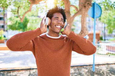 Genç yakışıklı Afro-Amerikan adam kulaklıkla müzik dinliyor. Yüzünde gülümsemeyle kasaba caddesinde yürürken.