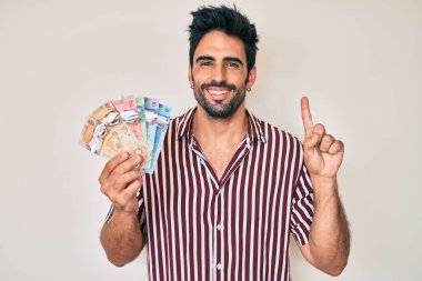 Sakallı yakışıklı İspanyol bir adam elinde Kanada doları ile bir fikir ya da soru işareti ile gülümsüyor. 