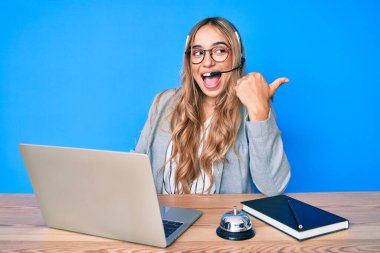 Çağrı merkezinde operatör kulaklığı takan genç ve güzel sarışın bir kadın baş parmağını yana kaldırıp ağzı açık gülümsüyor. 