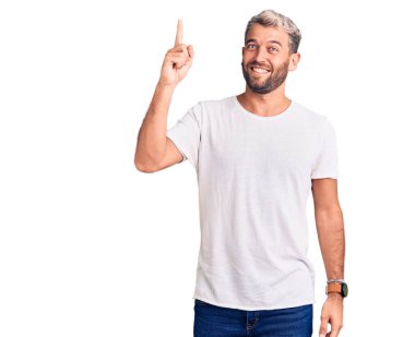 Gündelik tişörtler giyen genç, sarışın ve kafası karışık, kolları ve elleri havada bir adam. şüphe kavramı. 