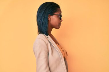 Afro-Amerikalı genç bir kadın iş kıyafetleri giyiyor. Taraf arıyor, rahat poz veriyor. Kendine güvenen bir gülümsemesi var.. 
