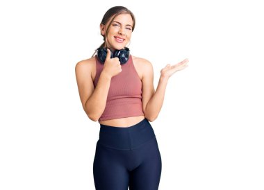 Güzel, beyaz, spor kıyafetleri giyen, kulaklık takan, el hareketlerini yapan, mutlu ve neşeli gülümseyen bir kadın. 