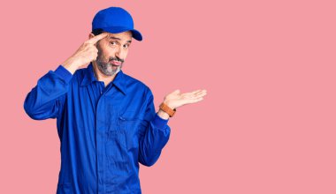 Orta yaşlı, tamirci üniforması giyen yakışıklı bir adam avuç içinin açık olmasından rahatsız ve kafası karışmış bir şekilde fotokopi alanını gösteriyor ve alnını işaret ediyor. Bunu bir düşün.. 