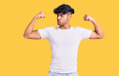 Sıradan kıyafetler giyen genç İspanyol adam gururla gülümseyen kol kaslarını gösteriyor. fitness konsepti. 