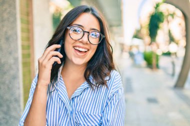 Genç İspanyol iş kadını gülümsüyor. Şehirdeki akıllı telefondan mutlu bir şekilde konuşuyor..