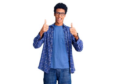 Sıradan kıyafetler ve gözlük takan genç Afro-Amerikan bir adam olumlu el hareketi yapıyor, gülümsüyor ve mutlu. Neşeli ifade ve kazanan jest. 