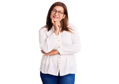 Orta yaşlı, gündelik kıyafetler ve gözlük takan, kameraya kendinden emin, kolları çapraz ve çenesi kalkık gülümseyen Latin bir kadın. Olumlu düşünmek. 