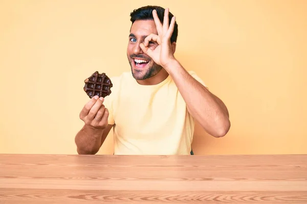 Joven Hombre Hispano Sosteniendo Gofre Chocolate Sentado Mesa Sonriendo Feliz — Foto de Stock