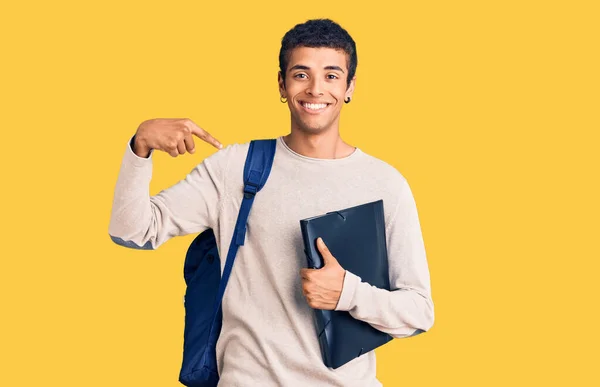 年轻的非洲裔美国人 背着学生背包 手里拿着活页夹 手指对着一个人 面带微笑 兴高采烈 — 图库照片