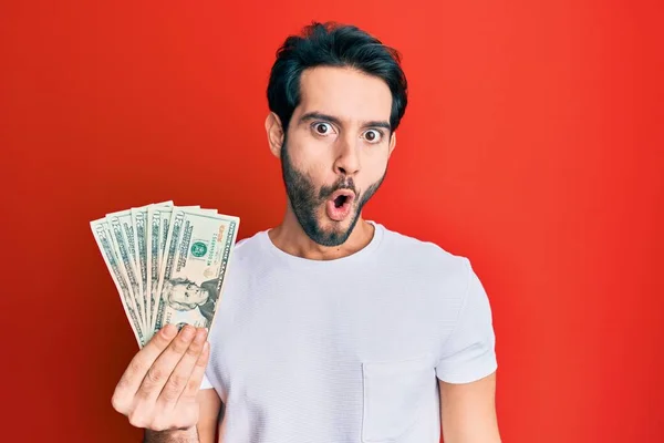 Young Hispanic Man Holding Dollars Banknote Scared Amazed Open Mouth — Stock Photo, Image
