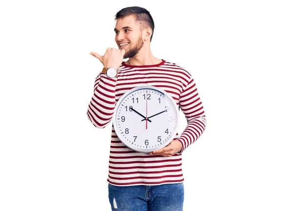 Jovem Homem Bonito Segurando Grande Relógio Apontando Polegar Até Lado — Fotografia de Stock