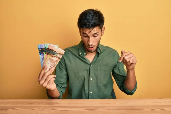 Joven Hombre Guapo Sosteniendo Dólares Canadienses Apuntando Hacia Abajo Con — Foto de Stock