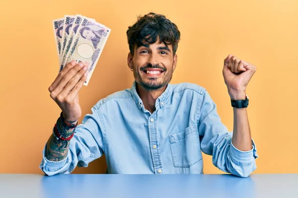 Jovem Hispânico Segurando Notas Iene Japonês Sentado Mesa Gritando Orgulhoso — Fotografia de Stock