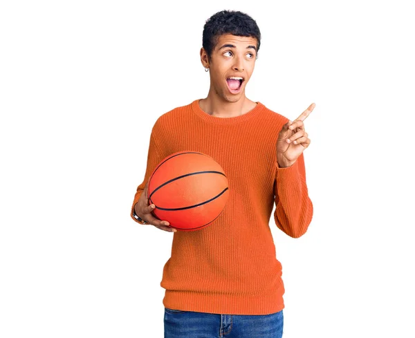 Joven Africano Amerciano Sosteniendo Pelota Baloncesto Apuntando Pulgar Hacia Lado — Foto de Stock