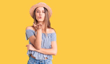 Şapka ve tişört giyen genç ve güzel bir kız kameraya bakıp havada bir öpücük savuruyor ve sevimli ve seksi oluyor. aşk ifadesi. 