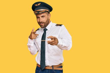 Uçak pilotu üniforması giyen sakallı yakışıklı adam kamerayı mutlu ve komik yüzüyle işaret ediyor. iyi enerji ve titreşimler. 