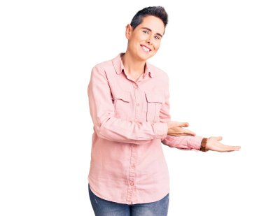 Kısa saçlı, günlük kıyafetler giyen genç bir kadın gülümseyerek içeri girmeye davet ediyor. 