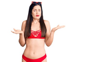 Bikinili, kafası karışık, kolları ve elleri havada genç, beyaz bir kadın. şüphe kavramı. 