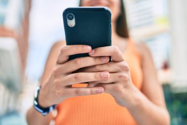 Ortadoğulu genç kız şehirde akıllı telefon kullanarak mutlu bir şekilde gülümsüyor..