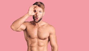 Beyaz bir genç, tişörtsüz bir şekilde ayakta duruyor. Şaşırmış bir yüz ve parmaklarından bakan bir gözle şaşırmış bir hareket yapıyor. İnançsız ifade. 