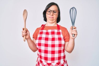 Esmer kadın, aşçı fırçası ve kaşıktan habersiz ve kafası karışmış bir ifadeyle yemek pişiriyor. şüphe kavramı. 