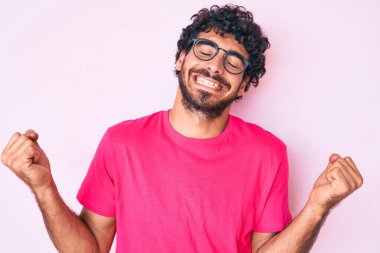 Kıvırcık saçlı ve ayı gibi giyinmiş yakışıklı genç bir adam. Çok mutlu ve heyecanlı. Kolları havada, gülümseyerek ve başarı için çığlık atarak kazanan jestler yapıyor. kutlama konsepti. 