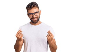 Gündelik kıyafetler ve gözlük takan genç İspanyol adam elleriyle para hareketi yapıyor, maaş istiyor, milyonerlik işi yapıyor. 