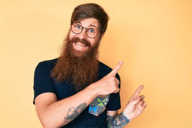 Uzun sakallı, sıradan giyinmiş, gözlüklü, gülümseyen ve kameraya bakan yakışıklı kızıl saçlı bir adam.. 