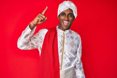 Sherwani sari giysisi giyen yakışıklı Hintli adam başarılı bir fikirle işaret ediyor. Heyecanlı ve mutlu. Bir numara.. 